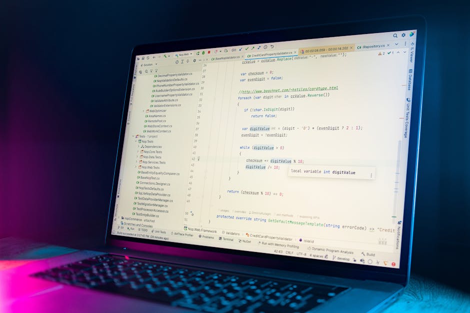 A close-up view of a laptop screen displaying lines of code, illuminated by blue and pink ambient lighting, set against a dark background. The code appears to be written in a programming language with